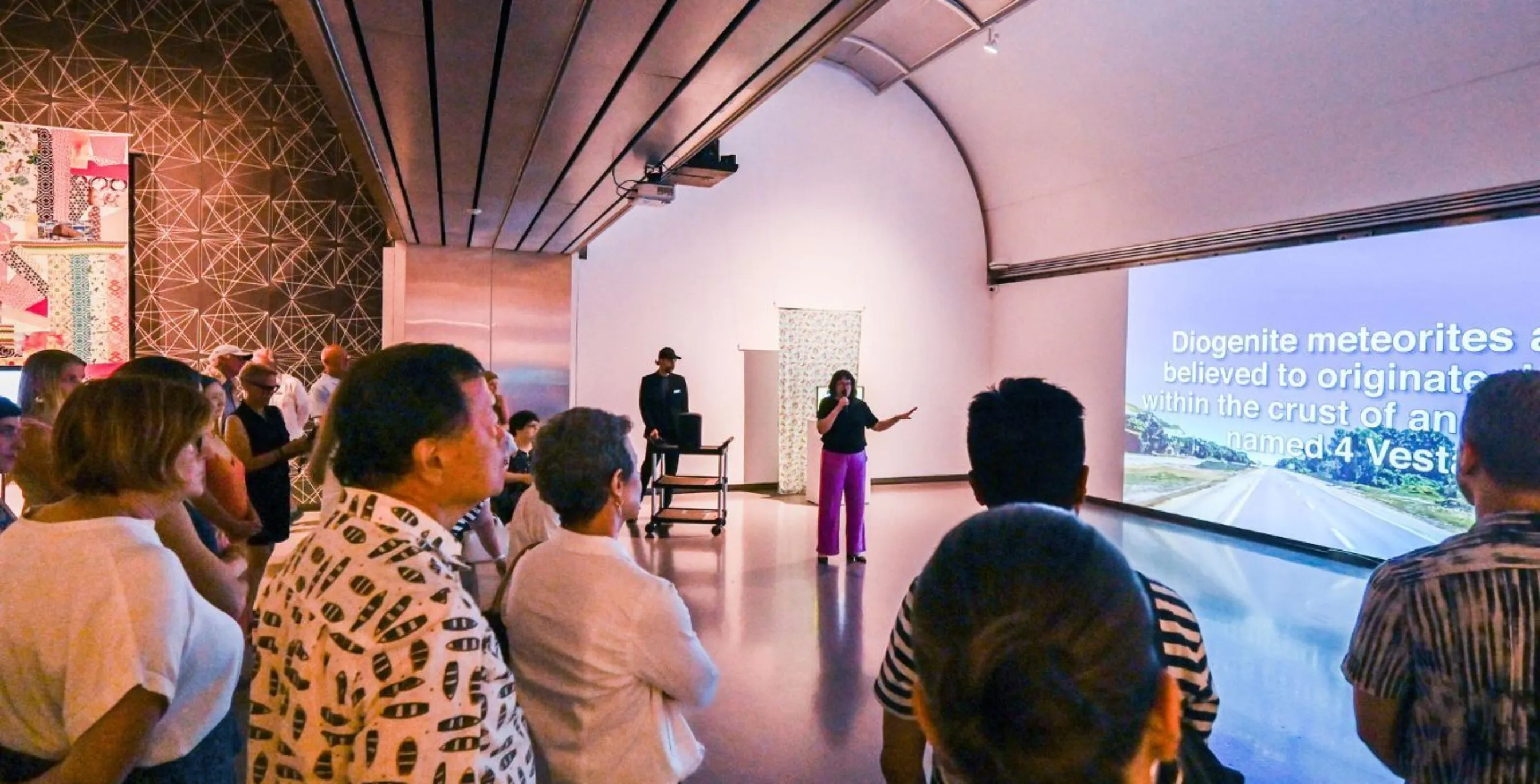 a crowd surrounds a curator in a gallery to learn about the artworks and artifacts on display