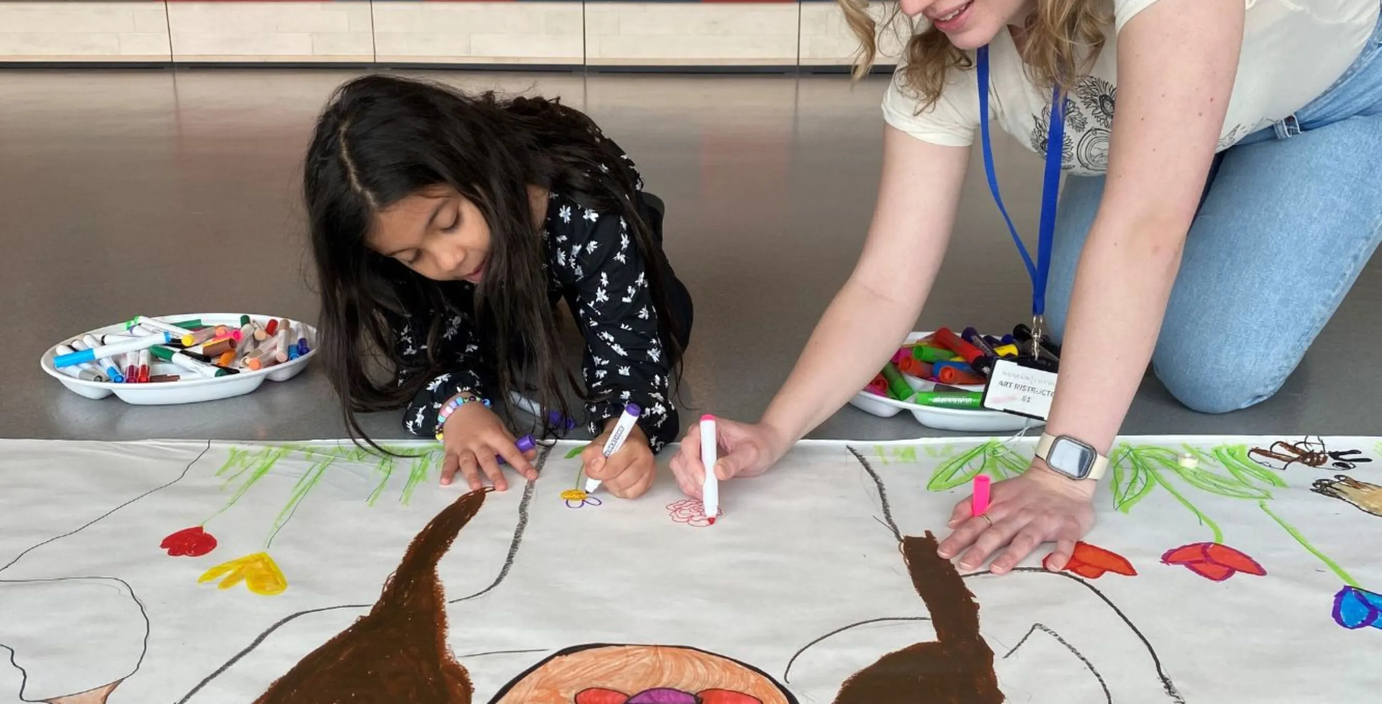 a school-aged child draws a larger than life character alongside an art instructor