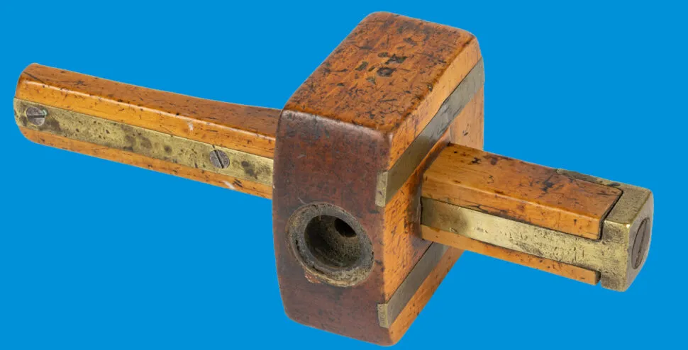 A historical moulding plane is seen on a vibrant blue background. The plan is made of wood and metal and shows signs of use over time.